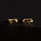 Pair of Pavé Viper Huggie Earrings in gold displayed on a dark surface, showcasing their wavy shape and pavé accents.