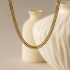 hick Mesh Chain Necklace in gold floats against a soft neutral backdrop. The lighting enhances the tightly interlocked mesh links, showcasing the necklace’s uniform weave