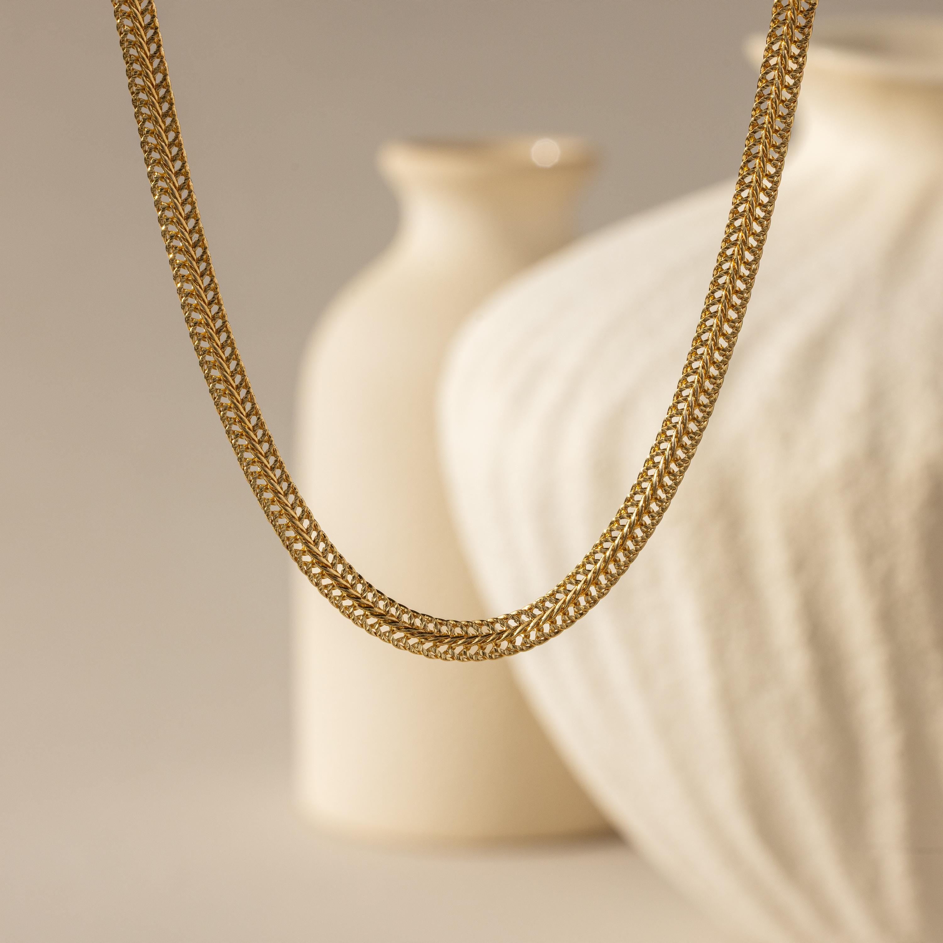 hick Mesh Chain Necklace in gold floats against a soft neutral backdrop. The lighting enhances the tightly interlocked mesh links, showcasing the necklace’s uniform weave