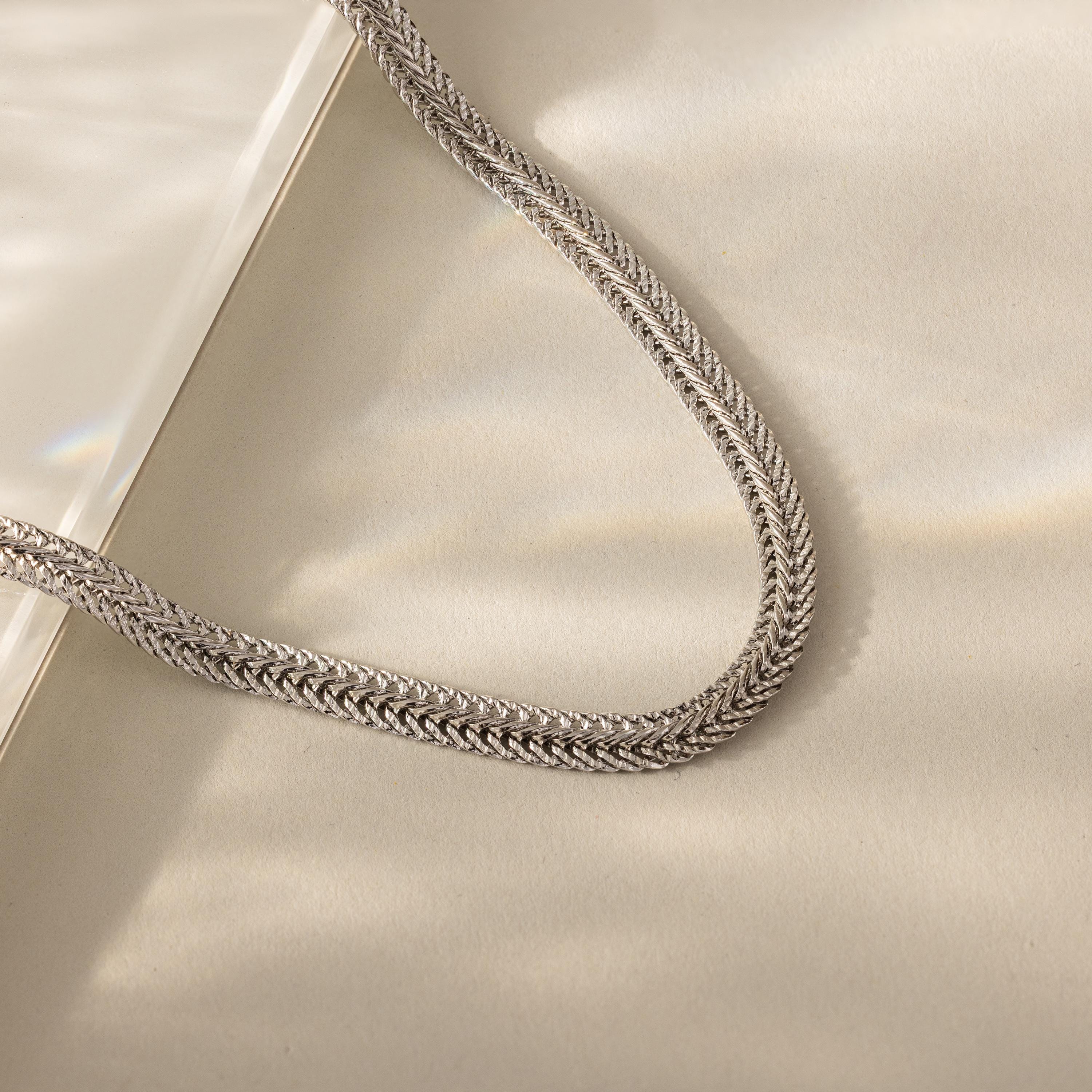 Close-up of a silver mesh chain necklace with intricate woven texture, displayed on a neutral background with soft lighting.