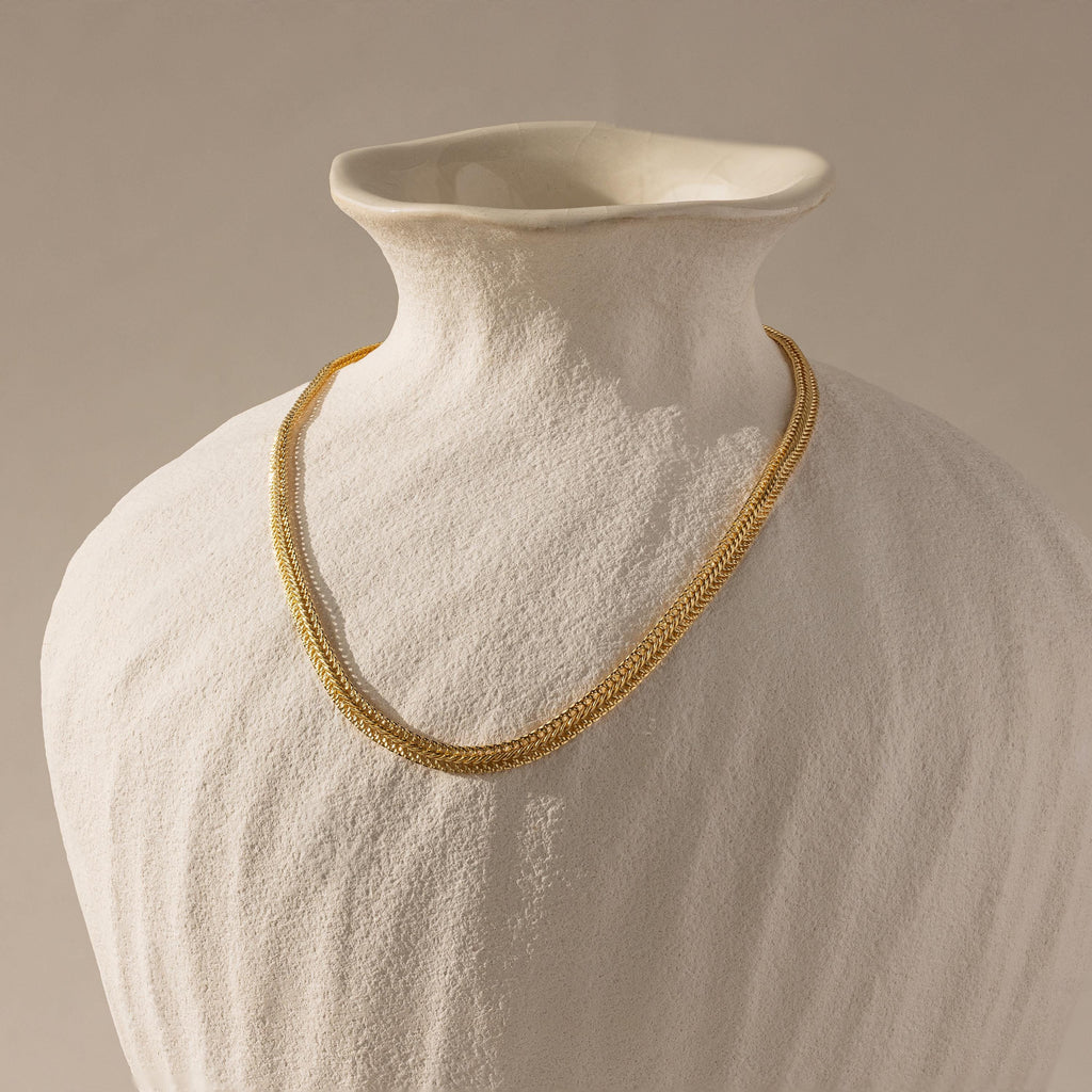 The gold mesh necklace displayed on a matte ceramic bust.