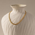 The gold mesh necklace displayed on a matte ceramic bust.