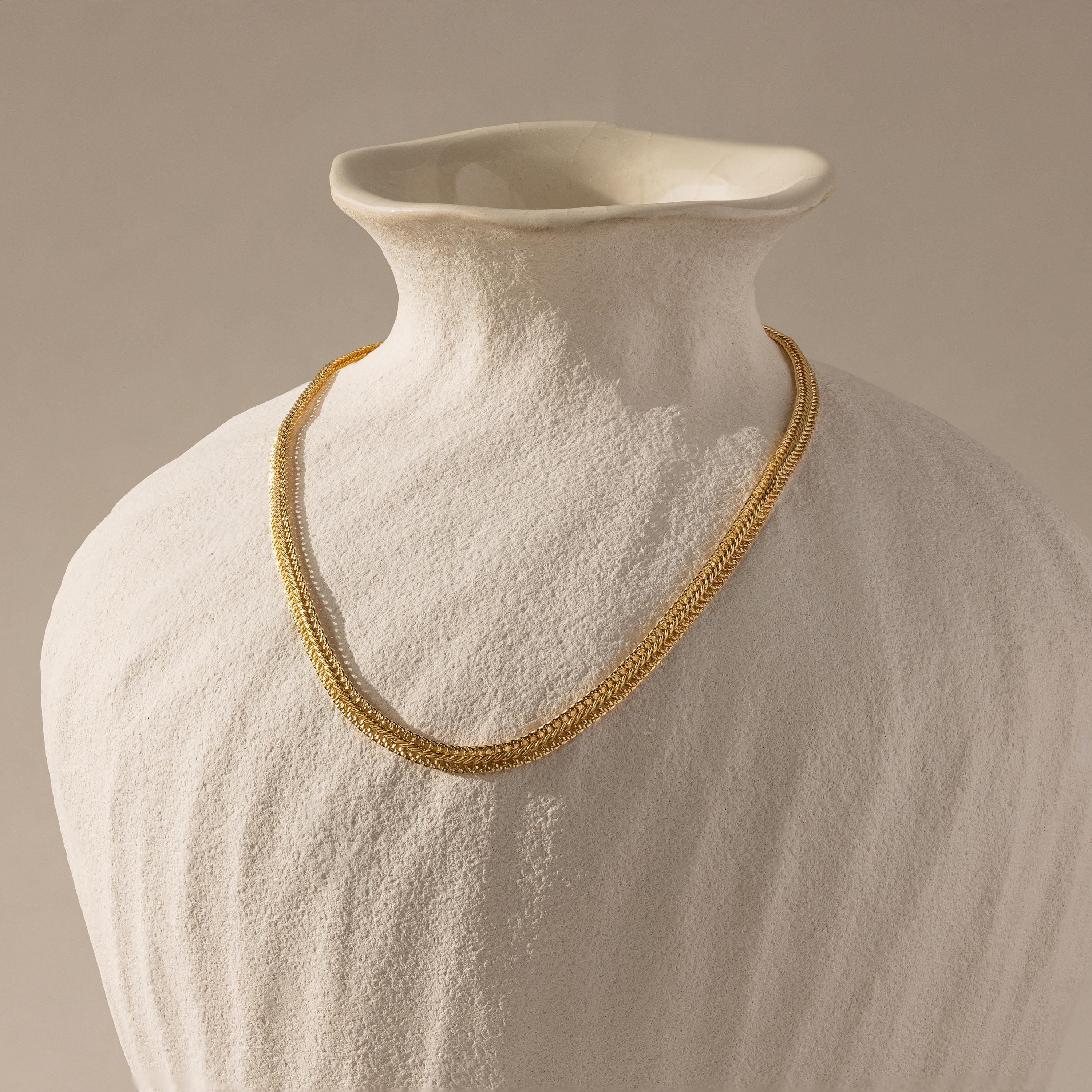 The gold mesh necklace displayed on a matte ceramic bust.