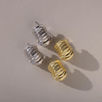 Aerial view of two pairs of chunky ribbed earrings—one in silver, one in gold—placed neatly with their posts visible and shadows cast beneath.
