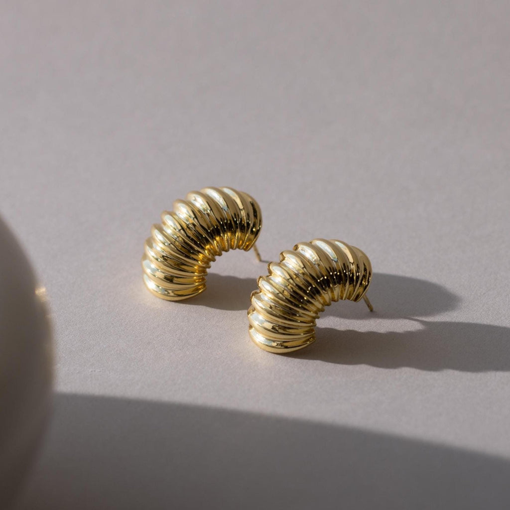 Pair of chunky ribbed earrings in 18K gold laid on a light surface