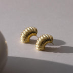 Pair of chunky ribbed earrings in 18K gold laid on a light surface