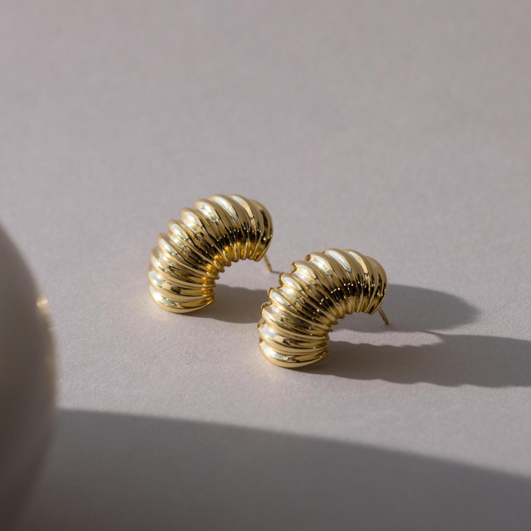 Pair of chunky ribbed earrings in 18K gold laid on a light surface