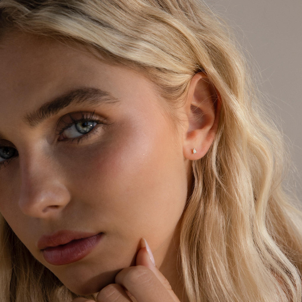 A silver pear opal stud styled on a model's ear, showing its understated elegance against fair skin and blonde hair.