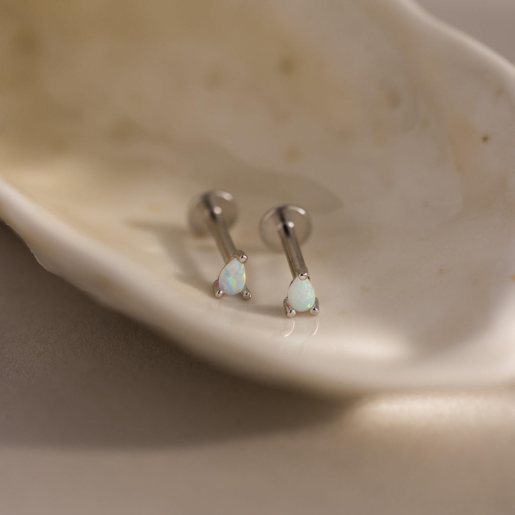 A close-up of a pair of silver pear opal flatback studs placed inside a smooth shell dish, highlighting the clean, modern finish.