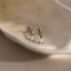 A close-up of a pair of silver pear opal flatback studs placed inside a smooth shell dish, highlighting the clean, modern finish.