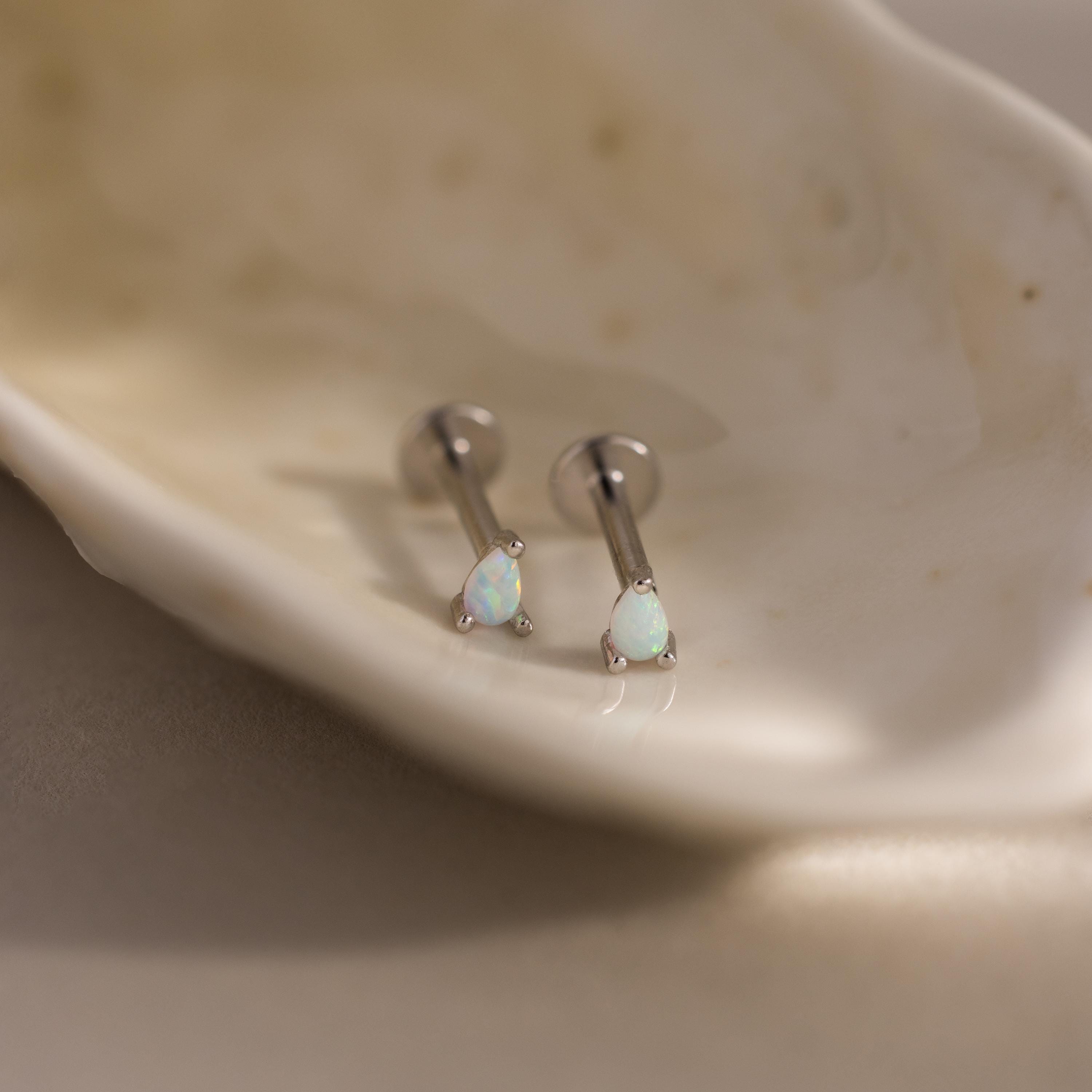A close-up of a pair of silver pear opal flatback studs placed inside a smooth shell dish, highlighting the clean, modern finish.