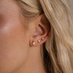 A close-up of a model wearing three earrings on one ear, including the gold pear opal stud, styled as part of a curated ear look.