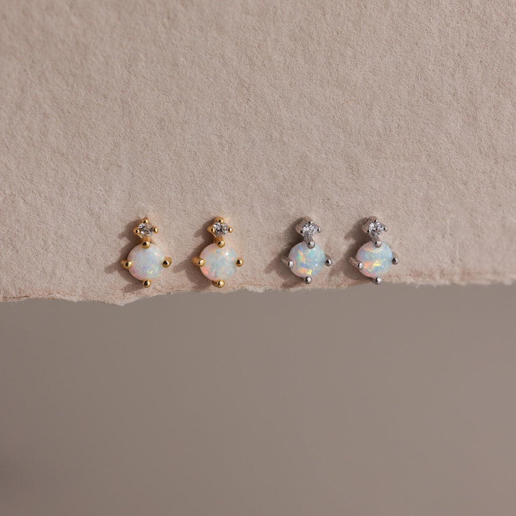 Two pairs of earrings — gold and silver — laid flat on textured beige paper.