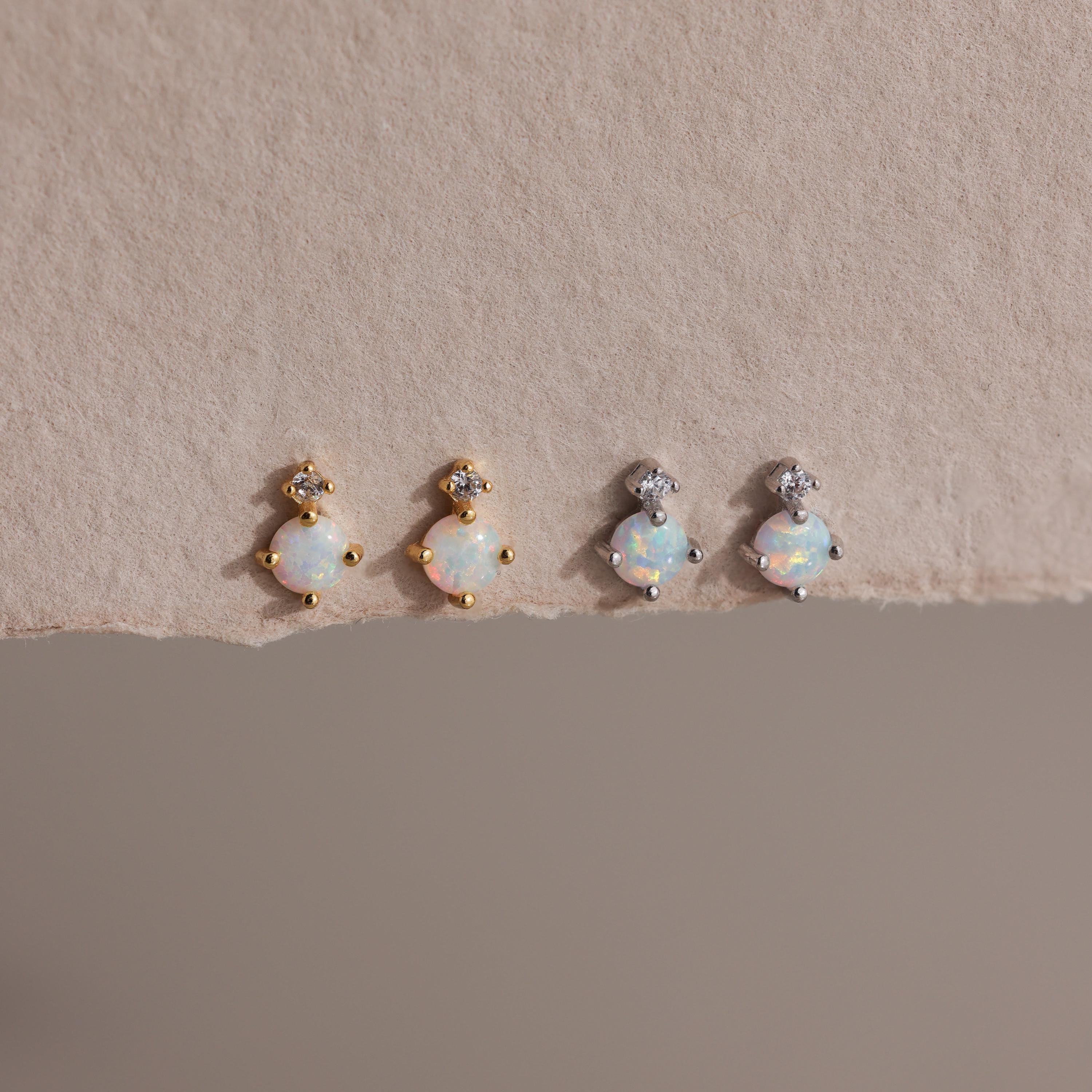 Two pairs of earrings — gold and silver — laid flat on textured beige paper.