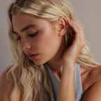 Model gently touching her hair while wearing the silver version of the opal and diamond earring.