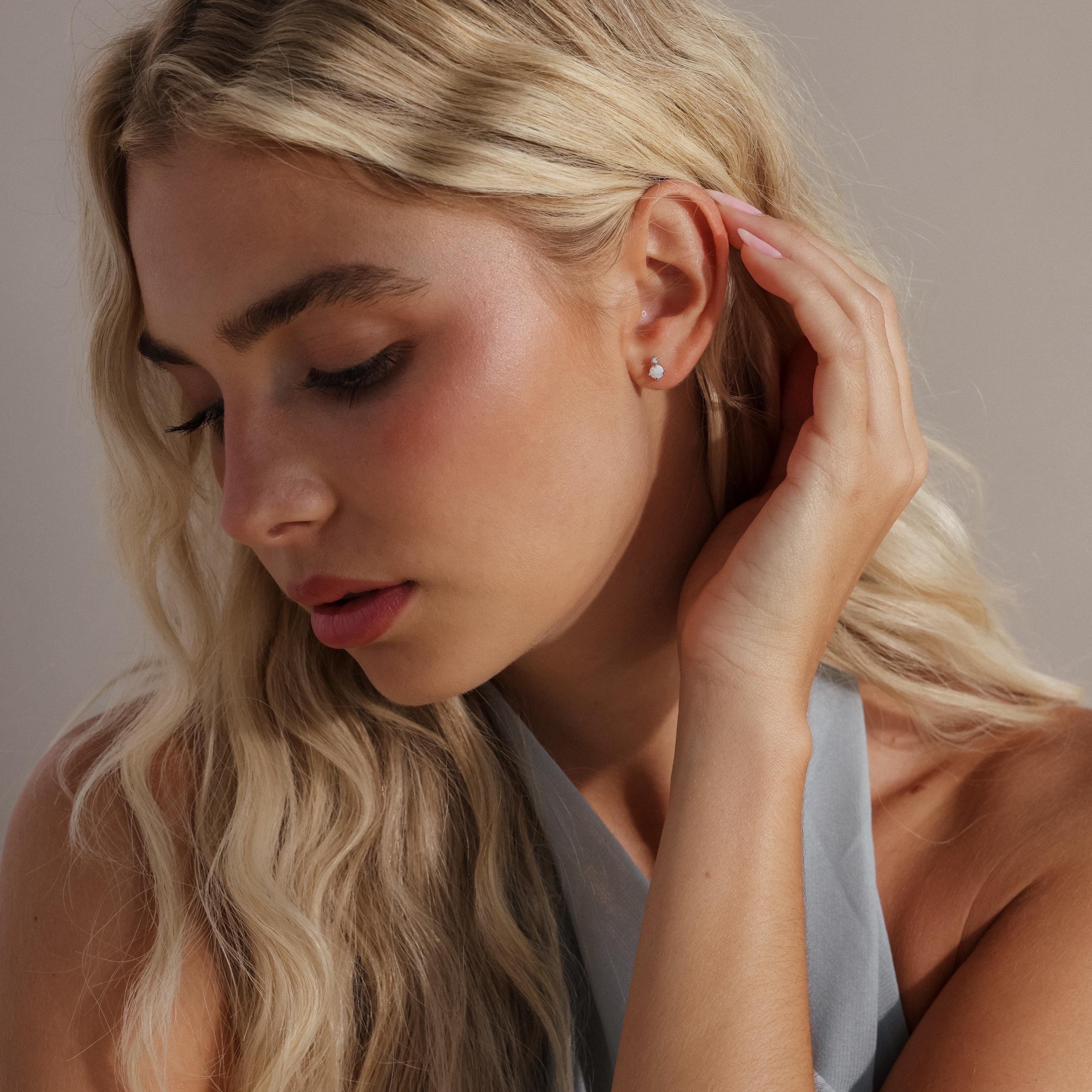 Model gently touching her hair while wearing the silver version of the opal and diamond earring.