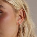 Close-up of a woman's ear with wavy blonde hair, wearing Opal & Diamond Flatback Studs that showcase the refined elegance of opal and diamond jewelry.