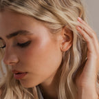 Side view of a model with blonde hair gently brushing her ear, wearing a single gold opal cluster stud earring on her lobe.