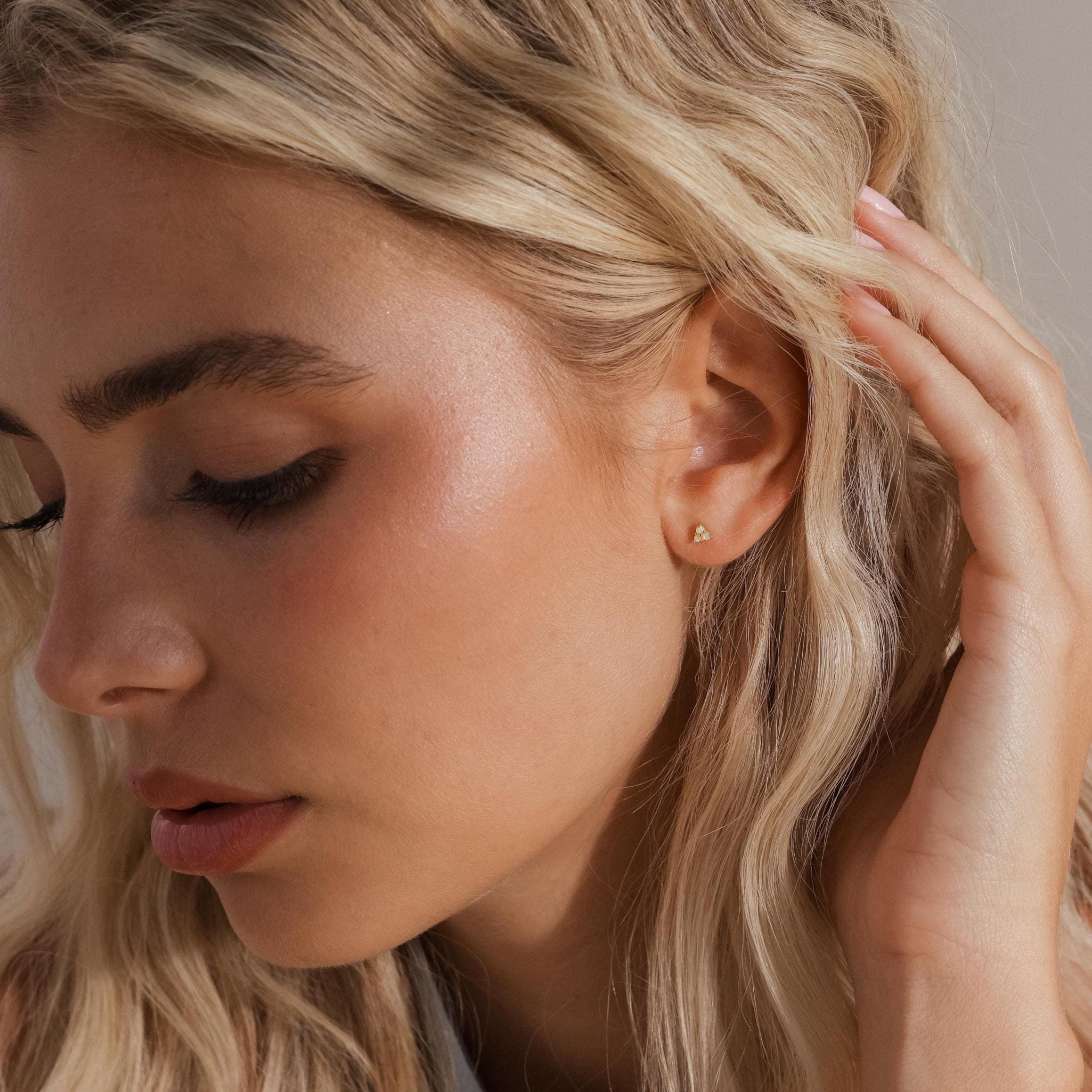 Side view of a model with blonde hair gently brushing her ear, wearing a single gold opal cluster stud earring on her lobe.