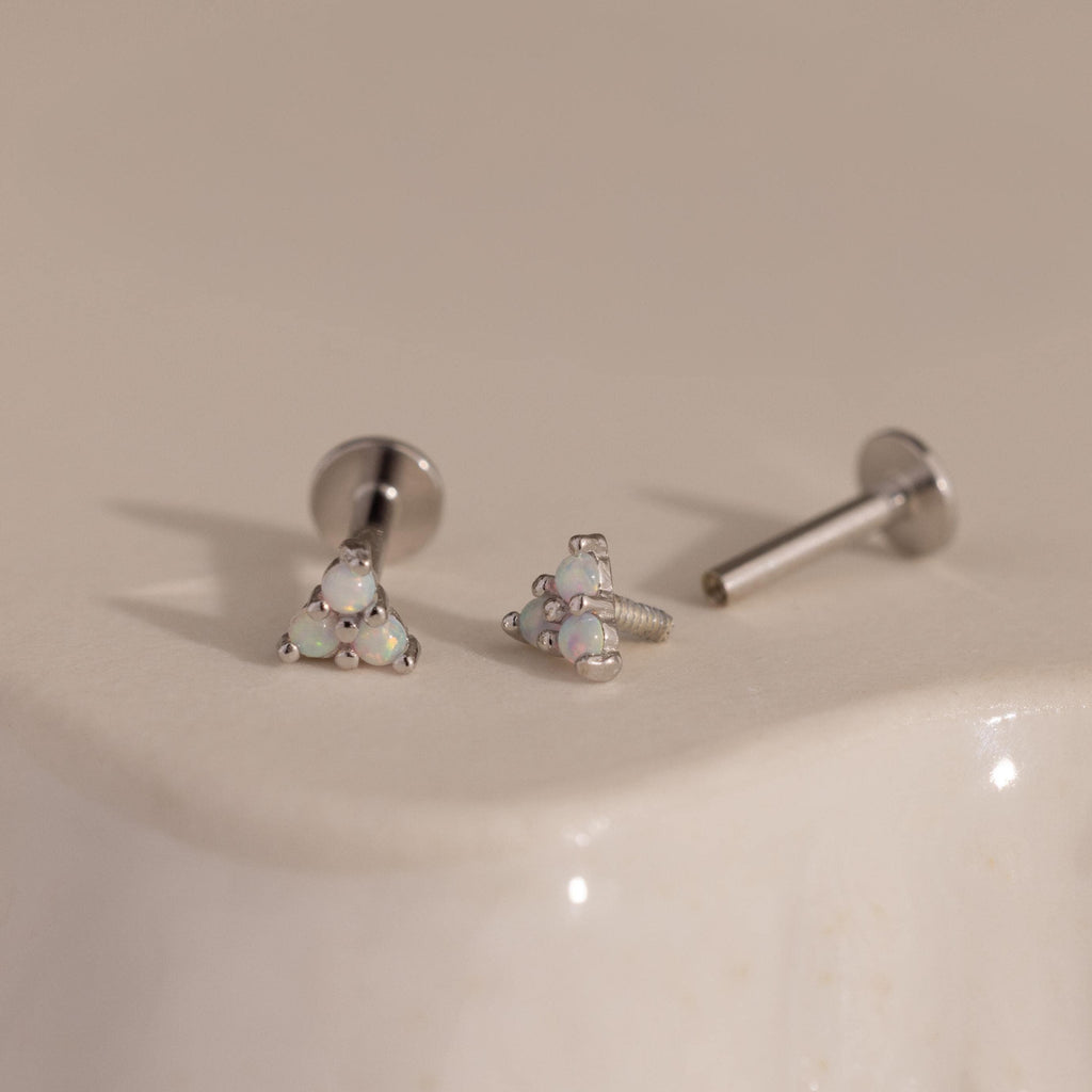 Three silver Opal Cluster Stud Earrings displayed on a smooth, light-colored ceramic surface, one showing the unscrewed post.