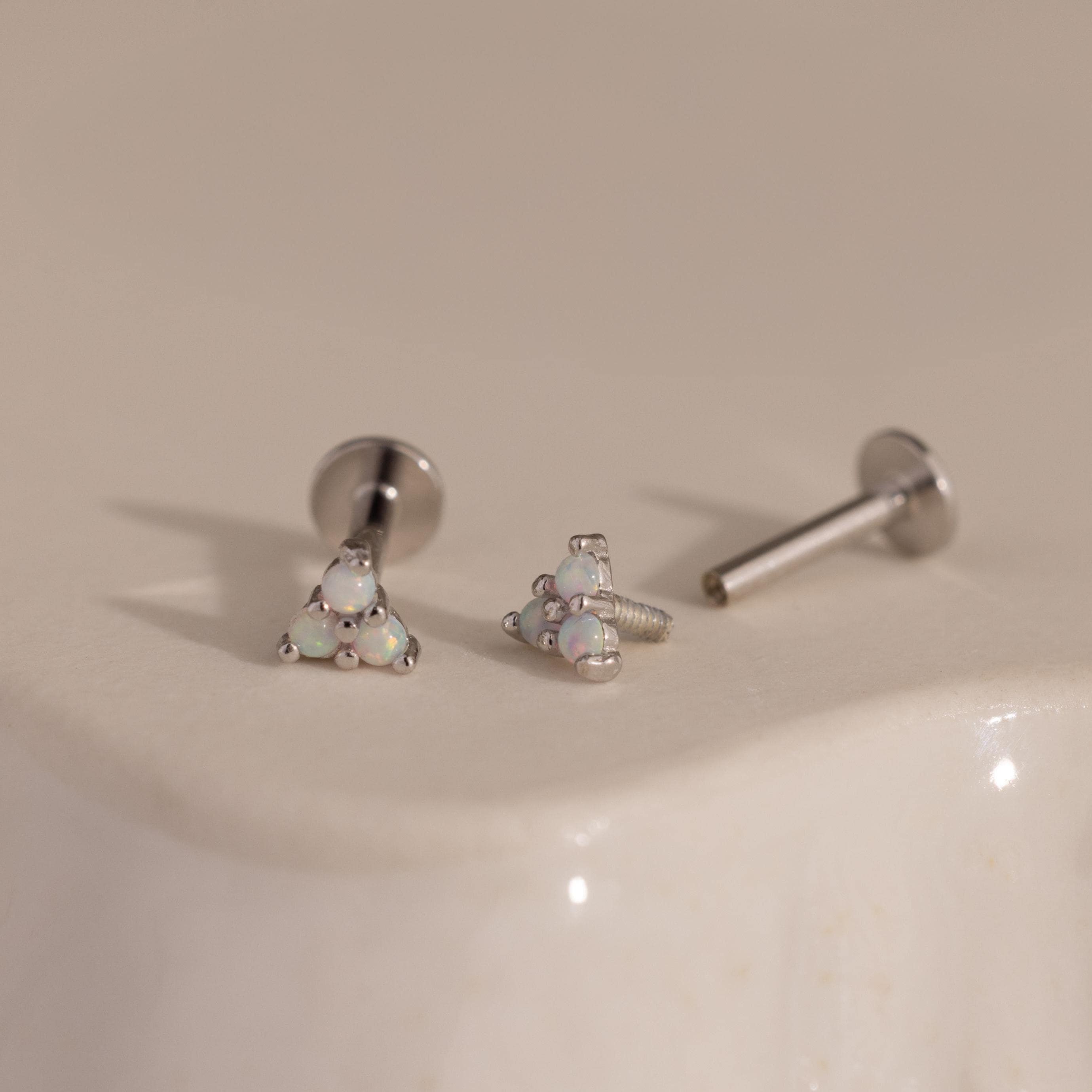 Three silver Opal Cluster Stud Earrings displayed on a smooth, light-colored ceramic surface, one showing the unscrewed post.