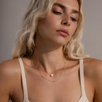 The Dainty Bow Necklace in gold layered with a pearl pendant necklace on a woman’s neck, demonstrating a delicate, stacked styling look.