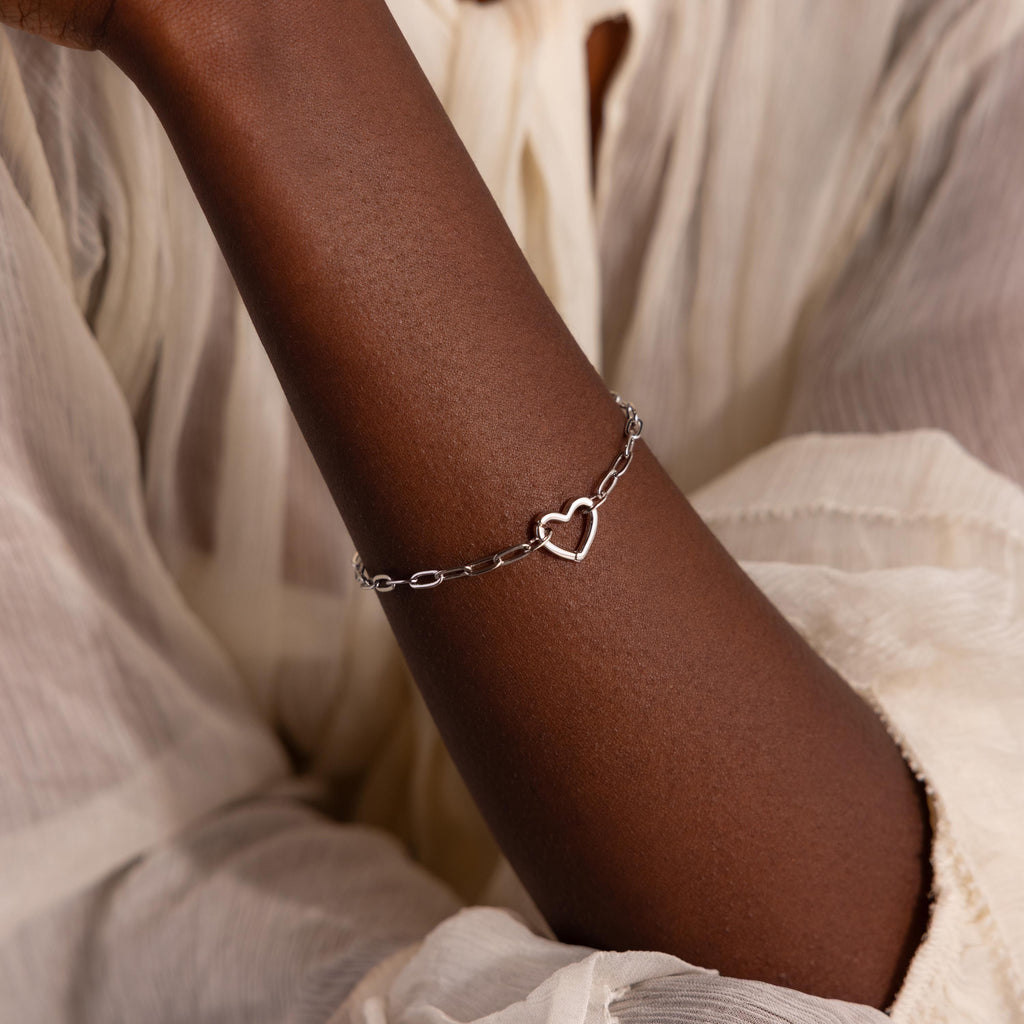 White gold version of the Heart Carabiner Paperclip Bracelet worn on wrist, styled with white blouse.