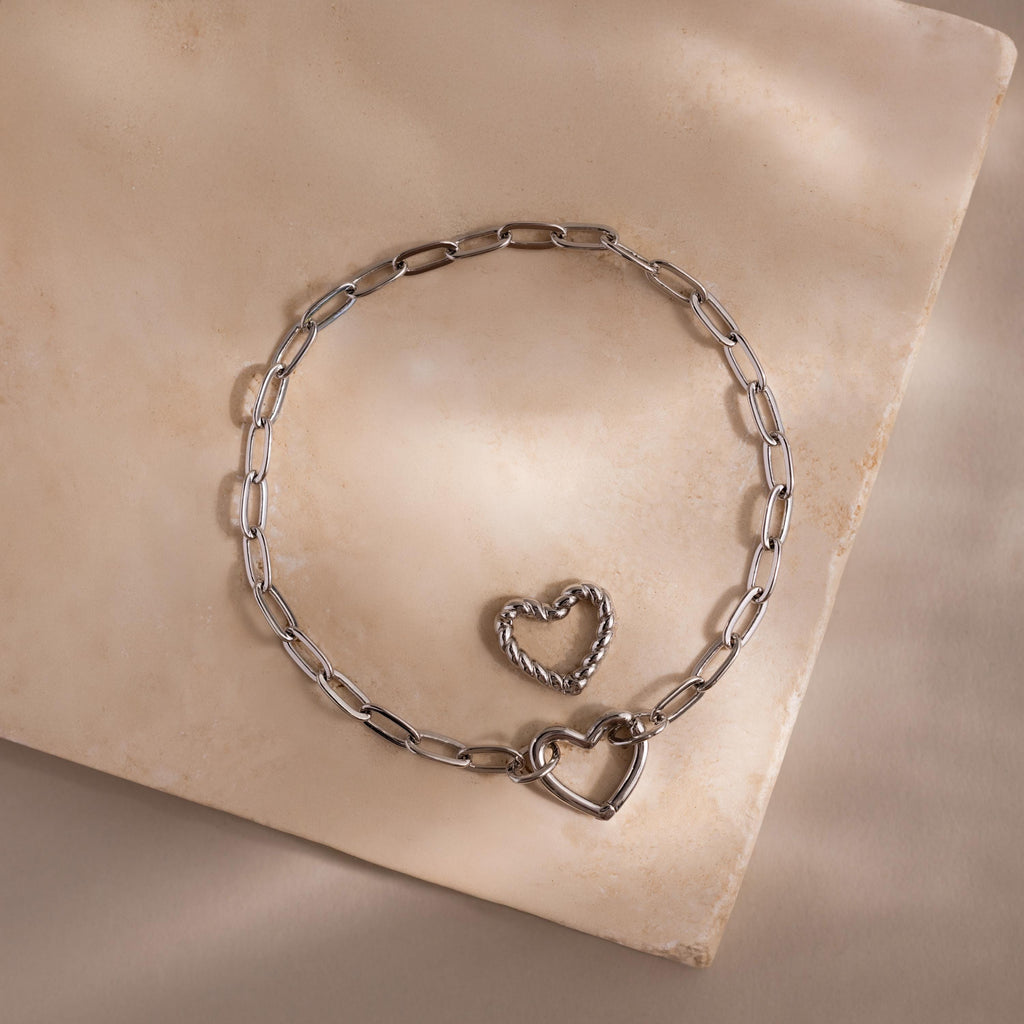 White gold Heart Carabiner Paperclip Bracelet with two interchangeable heart charms displayed on neutral stone.