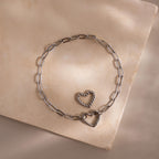 White gold Heart Carabiner Paperclip Bracelet with two interchangeable heart charms displayed on neutral stone.