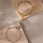 Flat lay of Heart Carabiner Paperclip Bracelets in gold and white gold on neutral-toned display blocks.