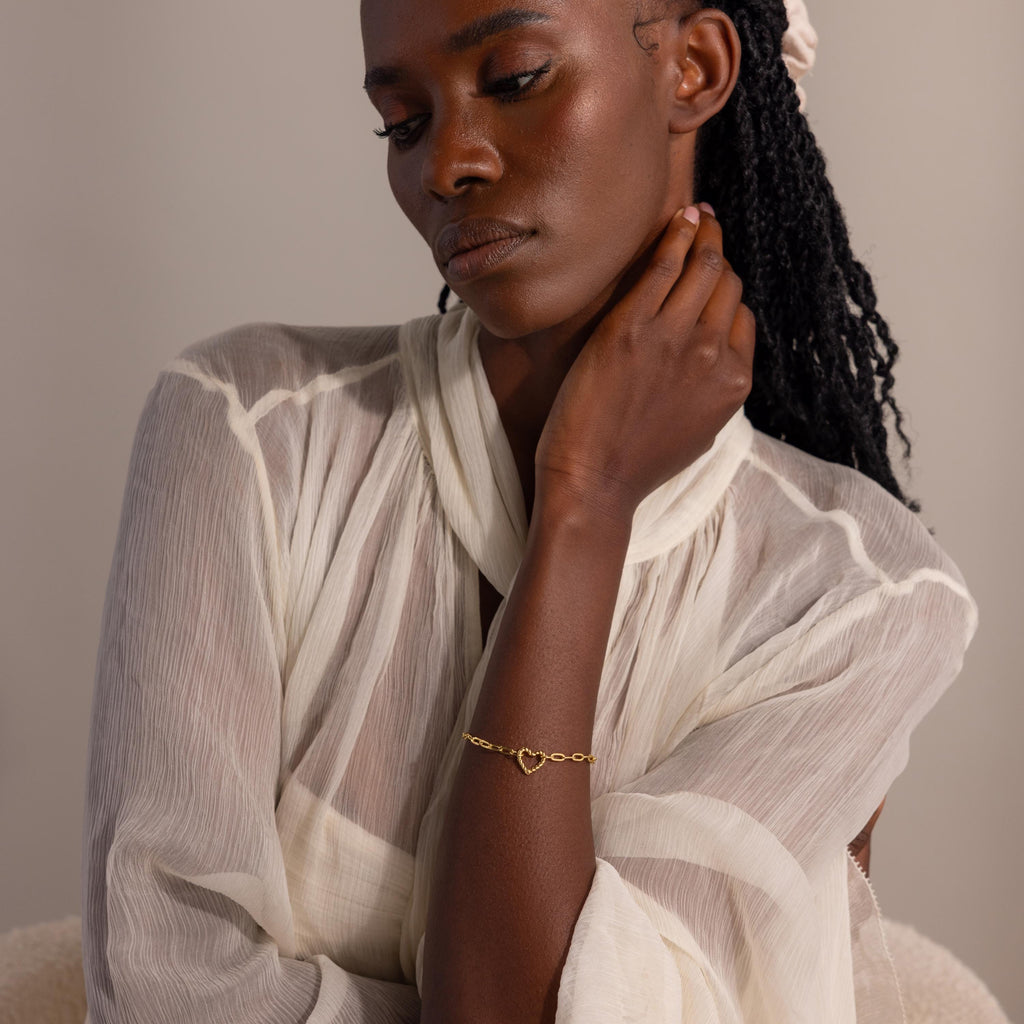 Model wearing the gold Heart Carabiner Paperclip Bracelet styled with sheer, pleated blouse.