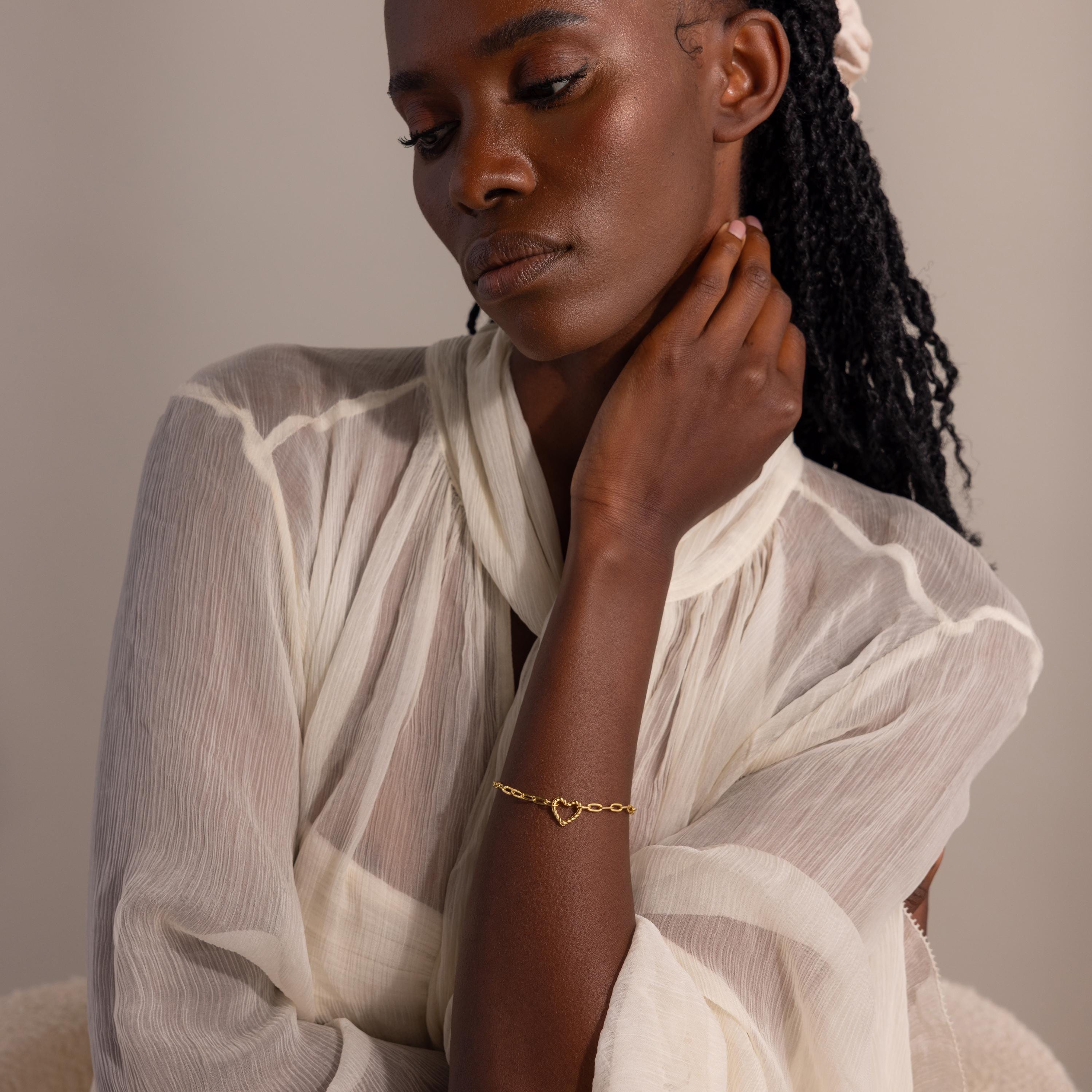 Model wearing the gold Heart Carabiner Paperclip Bracelet styled with sheer, pleated blouse.