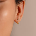 A close-up view of a woman's ear adorned with a gold flat back earring featuring two vertically aligned, four-pointed star charms. The top star sits snugly against the earlobe, while the second star dangles just below, catching the light with a polished gold finish.