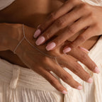 Woman's hands with soft pink nails wearing a dainty silver hand chain bracelet that loops around the finger and wrist.