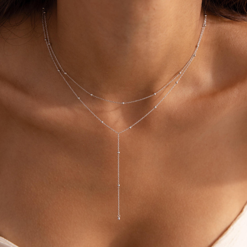 Close-up of a silver lariat necklace with double satellite chains resting on a woman’s collarbone.