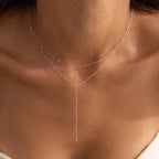 Close-up of a silver lariat necklace with double satellite chains resting on a woman’s collarbone.