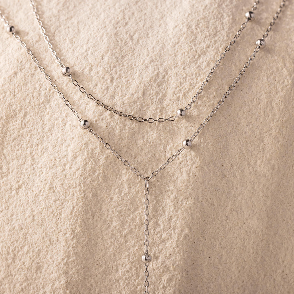 Close-up of the necklace’s gold satellite bead chain against a textured cream background.