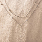 Close-up of the necklace’s gold satellite bead chain against a textured cream background.