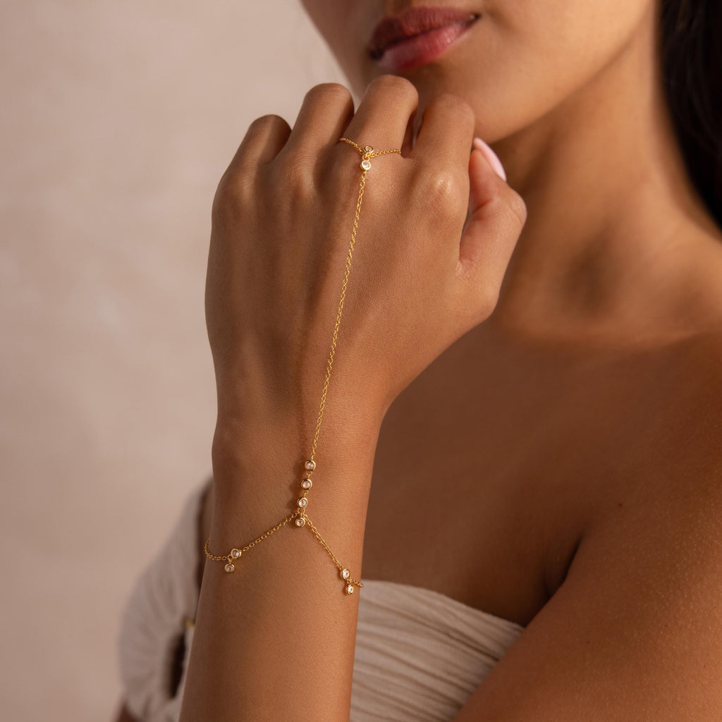 Woman wearing a delicate gold hand chain bracelet with bezel-set diamonds.