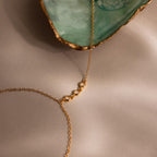 Close-up of three bezel-set diamonds on a gold chain next to a green and gold-edged seashell.