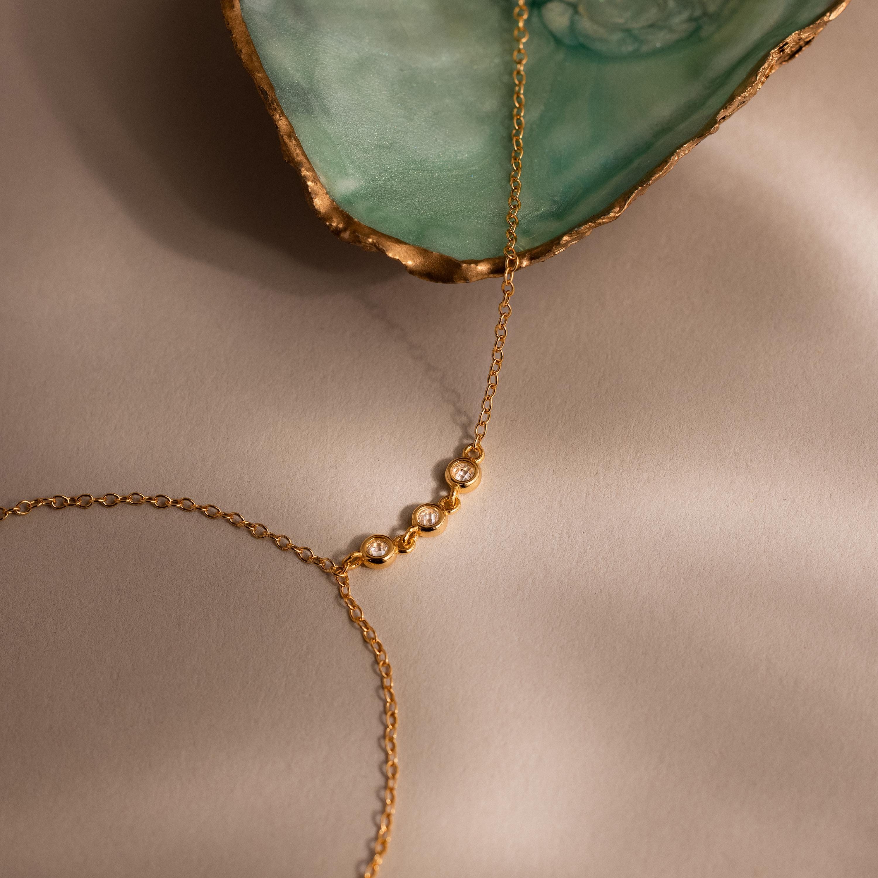 Close-up of three bezel-set diamonds on a gold chain next to a green and gold-edged seashell.