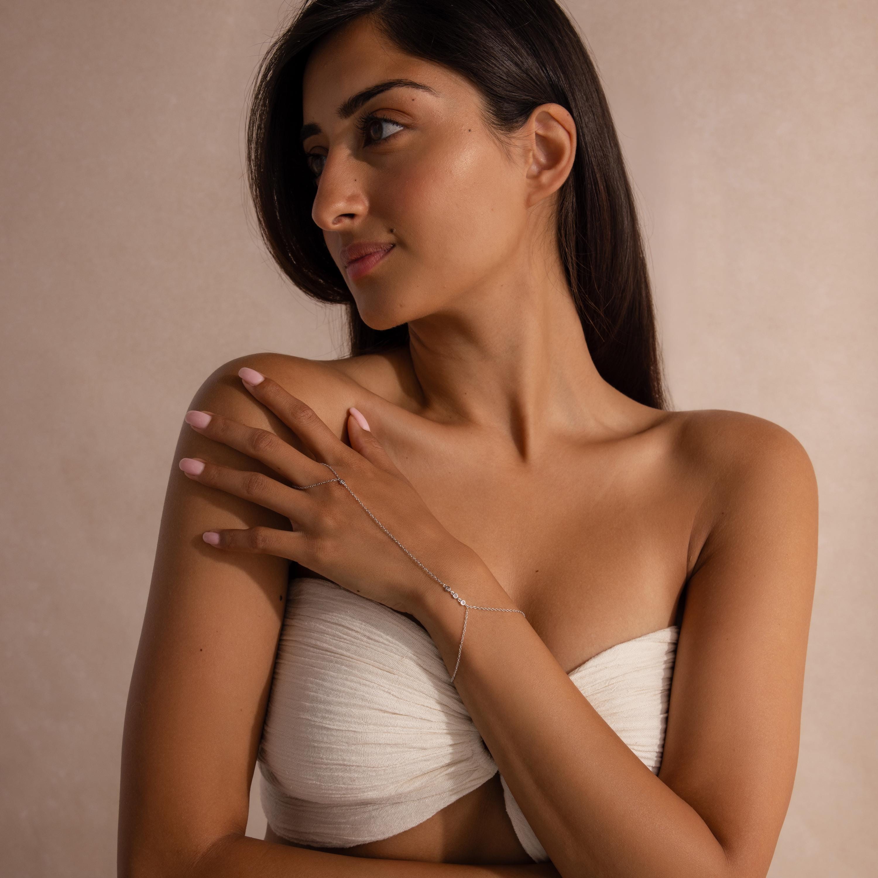 Close-up of a woman’s hand wearing a minimalist silver hand chain bracelet, with the chain extending from finger to wrist, styled with a neutral background.