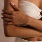 A silver hand chain bracelet with delicate diamonds laid flat on a beige surface with soft shadows.