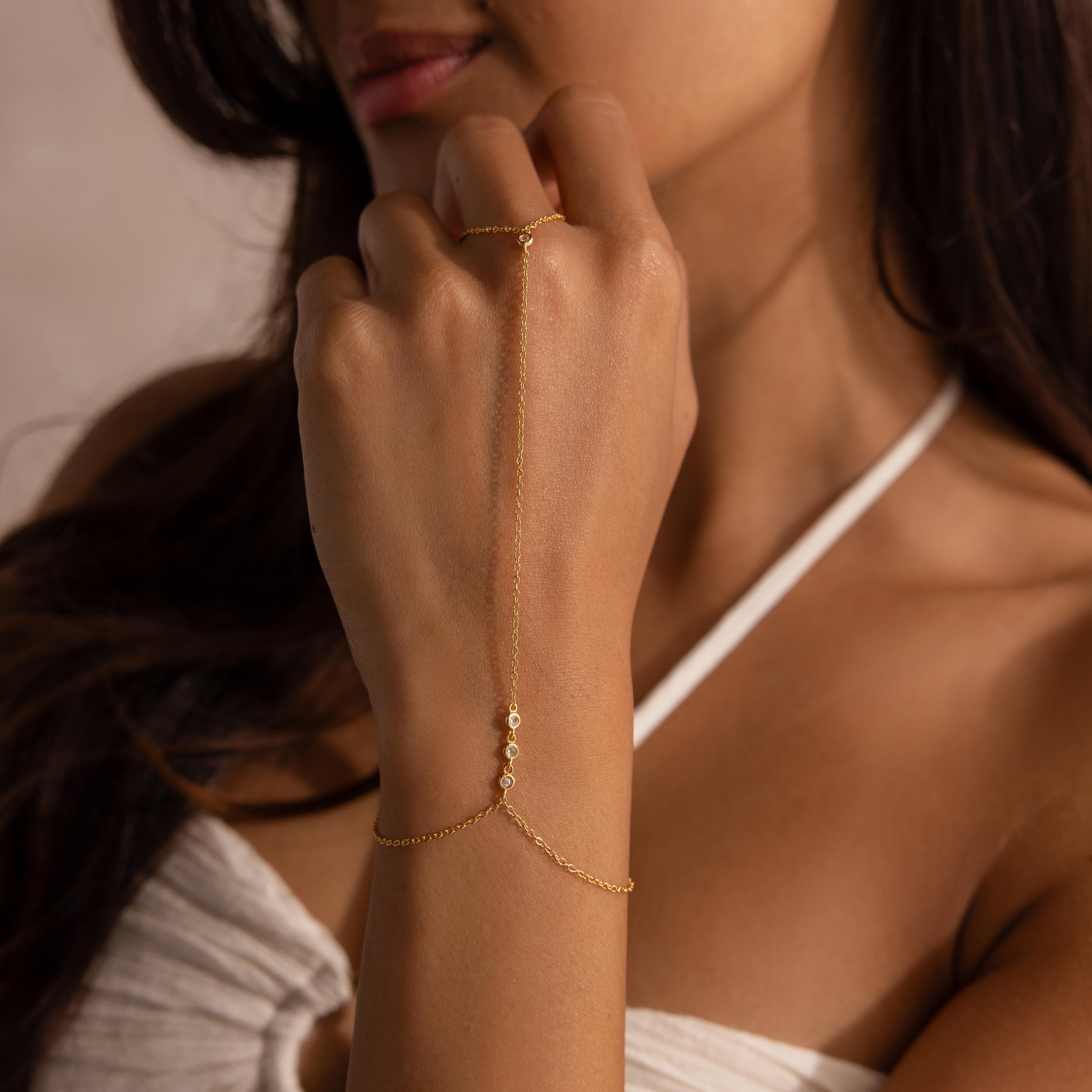Model resting her chin on her hand, highlighting the diamond-accented gold hand chain.