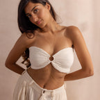 Woman wearing a gold body chain styled through the center of a white bandeau top, layered gracefully along her waist with pleated cream pants.