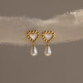 Pair of gold beaded heart earrings with mother-of-pearl centers and dangling pearls displayed on a soft textured fabric.