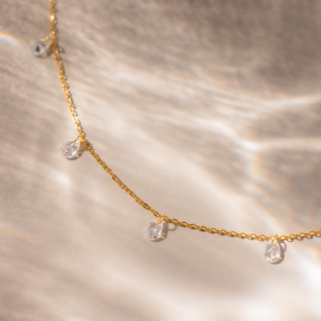 Close-up of the gold teardrop necklace laid flat on a neutral surface with soft lighting.