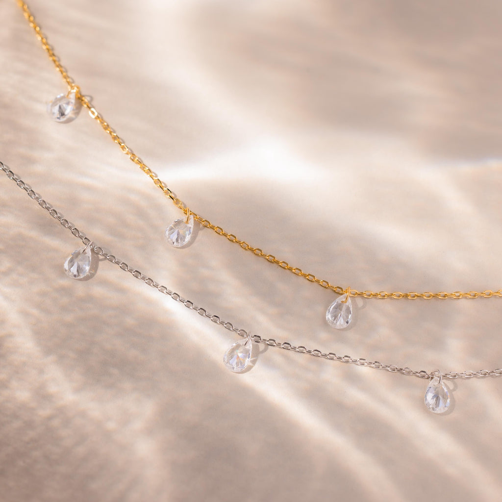Gold and silver teardrop necklaces laid side-by-side with the light highlighting the shine of the stones