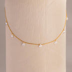 Diamond teardrop station necklace in gold draped around a textured cylindrical display in soft lighting.