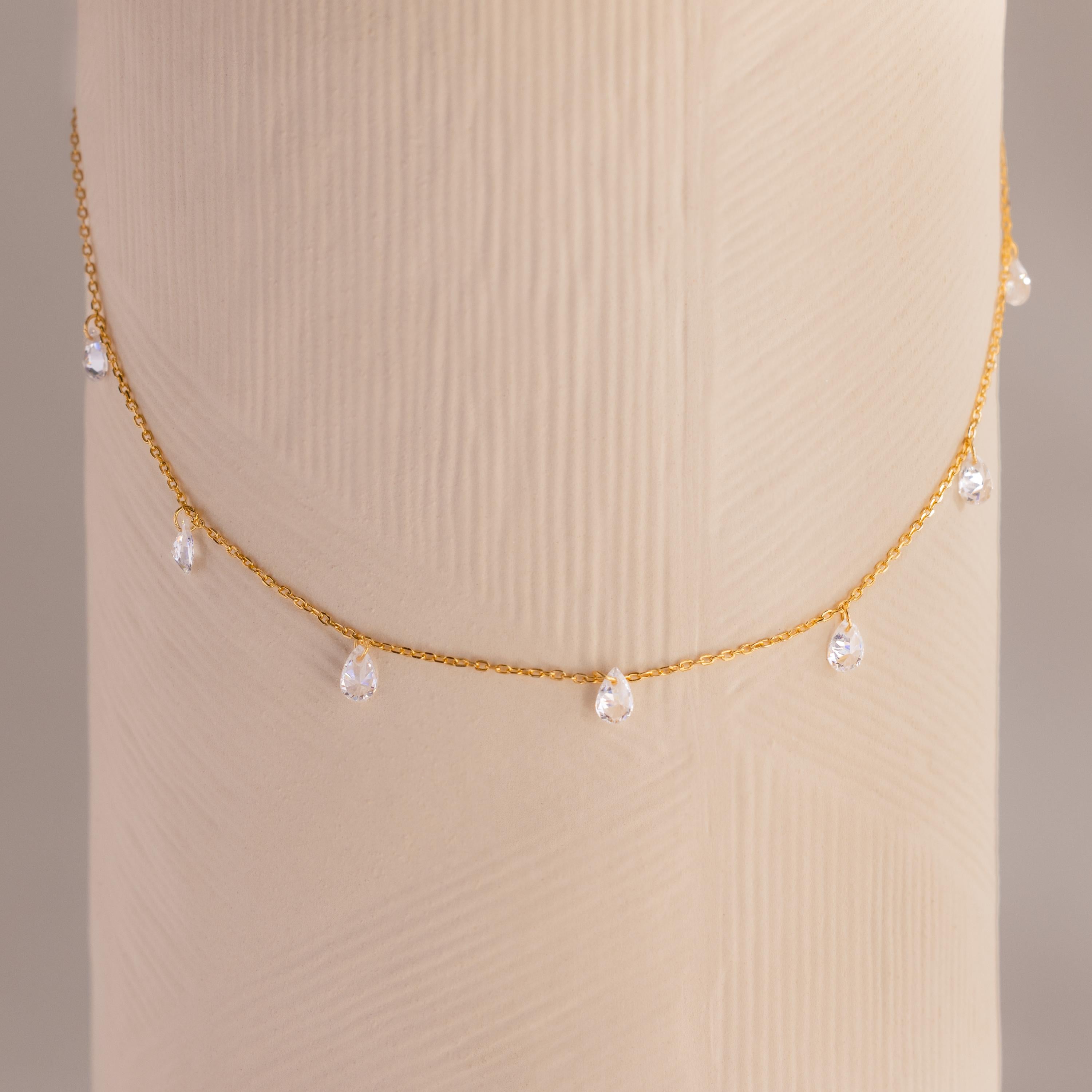 Diamond teardrop station necklace in gold draped around a textured cylindrical display in soft lighting.